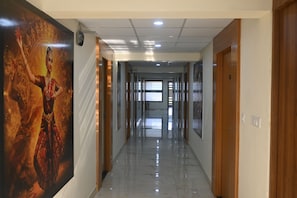 A hotel corridor with a long hallway, wooden doors, and a large poster on the left wall. - Reunion D Square Hotels & Resorts (Kundapur)