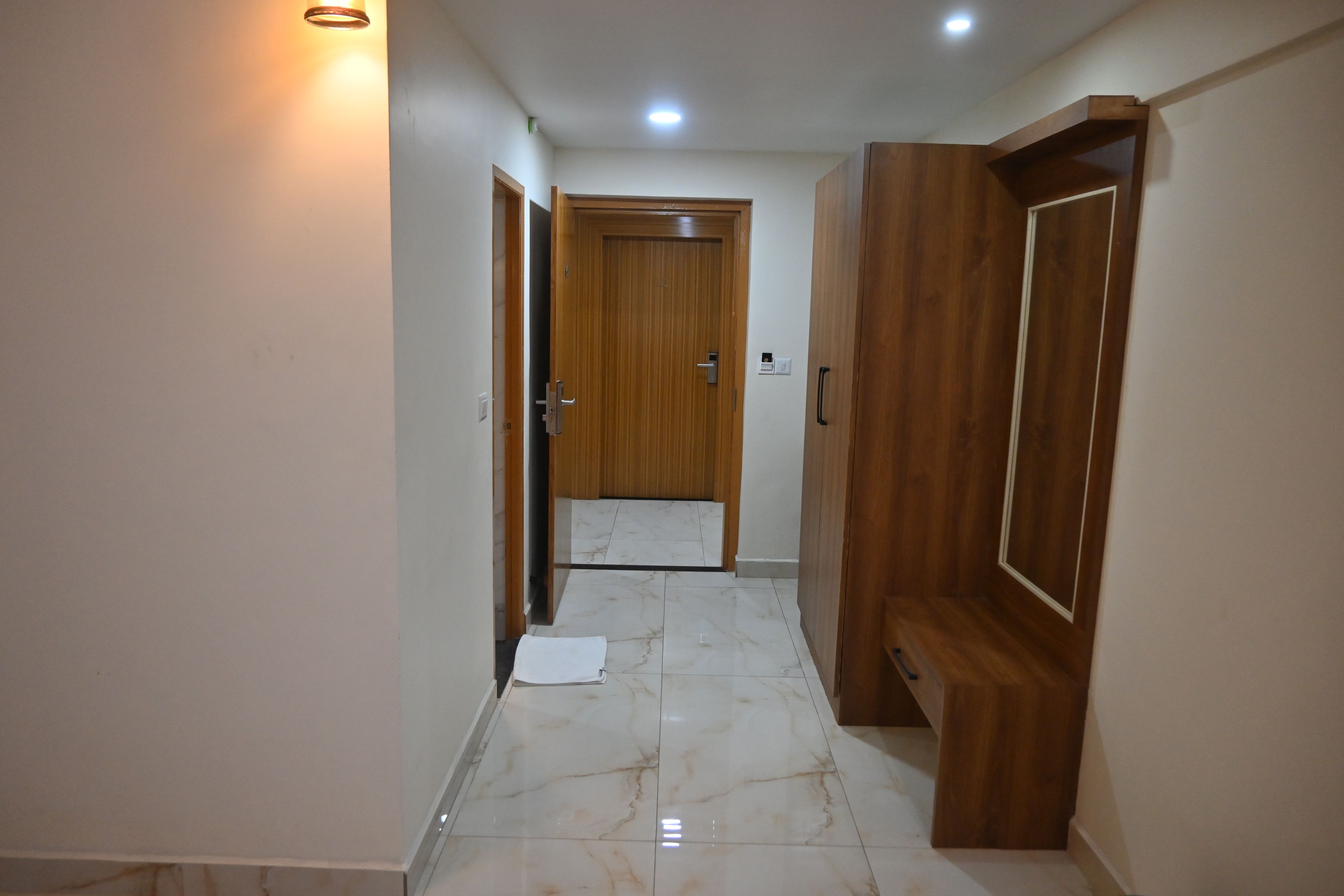 A hallway with a wooden door at the end, a light switch, and a small mat on the floor.
