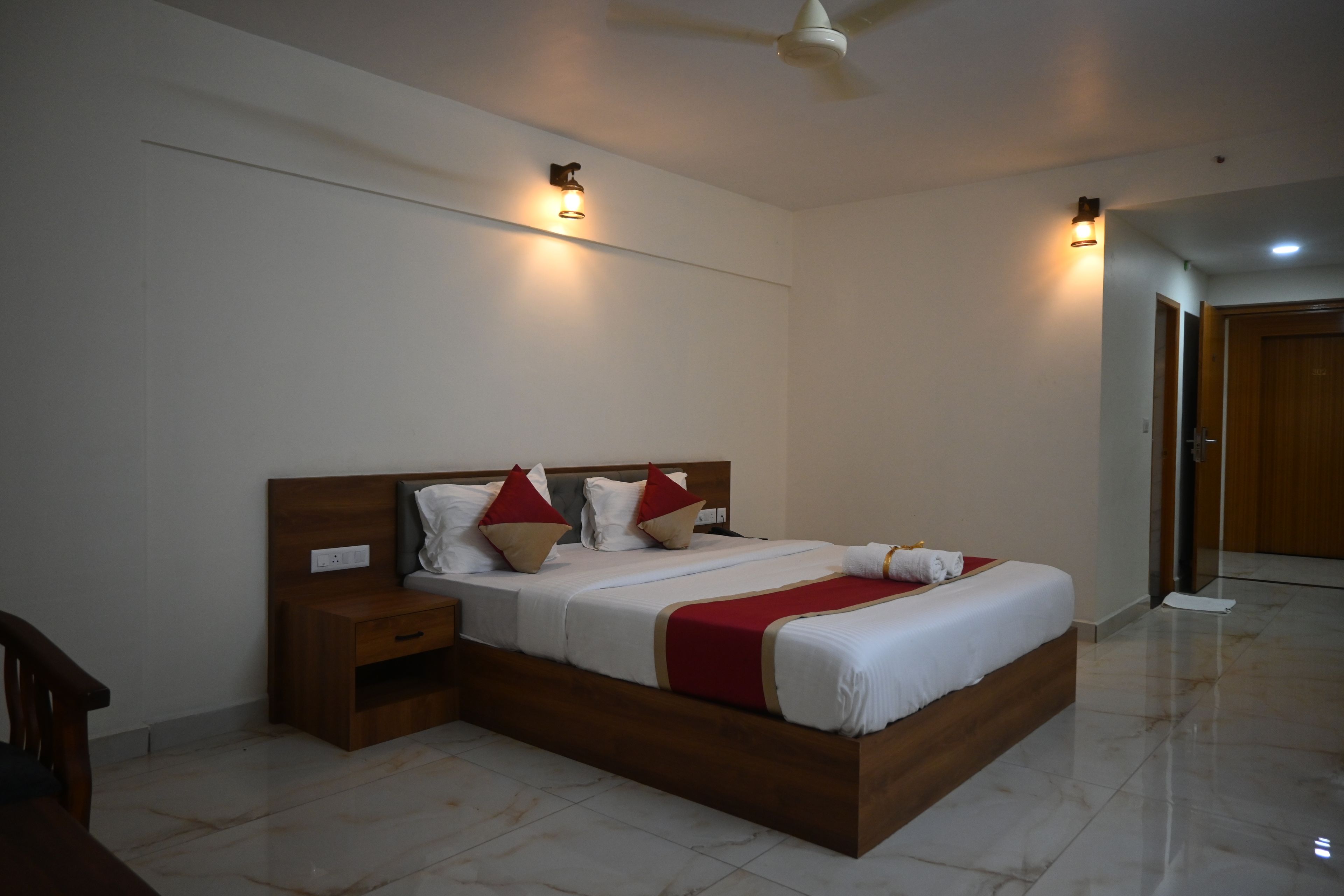 A hotel room with a large bed, bedside tables, a ceiling fan, and wall-mounted lighting.
