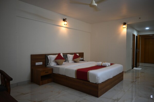 Habitación de hotel con una cama grande, mesitas de noche, ventilador de techo e iluminación empotrada.