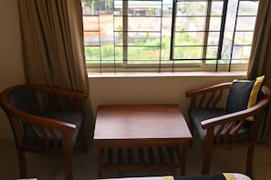 A room with a wooden table and two chairs, a window with a view of a green landscape, and a curtain on the left.