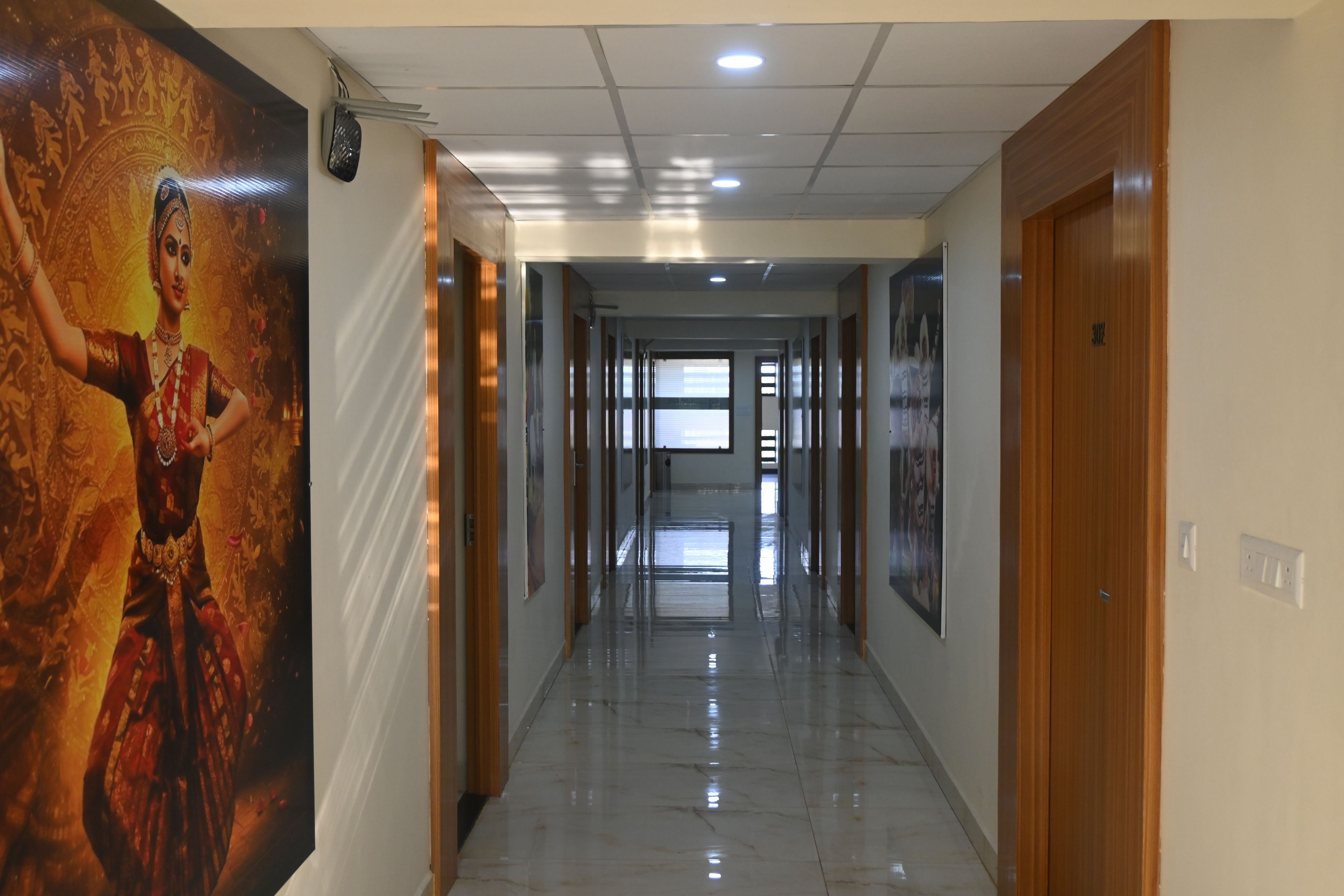 A corridor with a polished floor, wooden doors, and framed artwork on the walls.