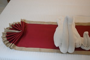 A bed with a red and beige bedspread, a white pillow, and a white towel.