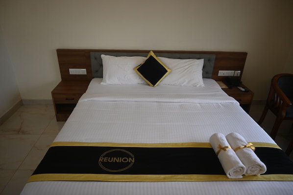 A hotel room with a neatly made bed, a bedside table, a chair, and a wall socket.