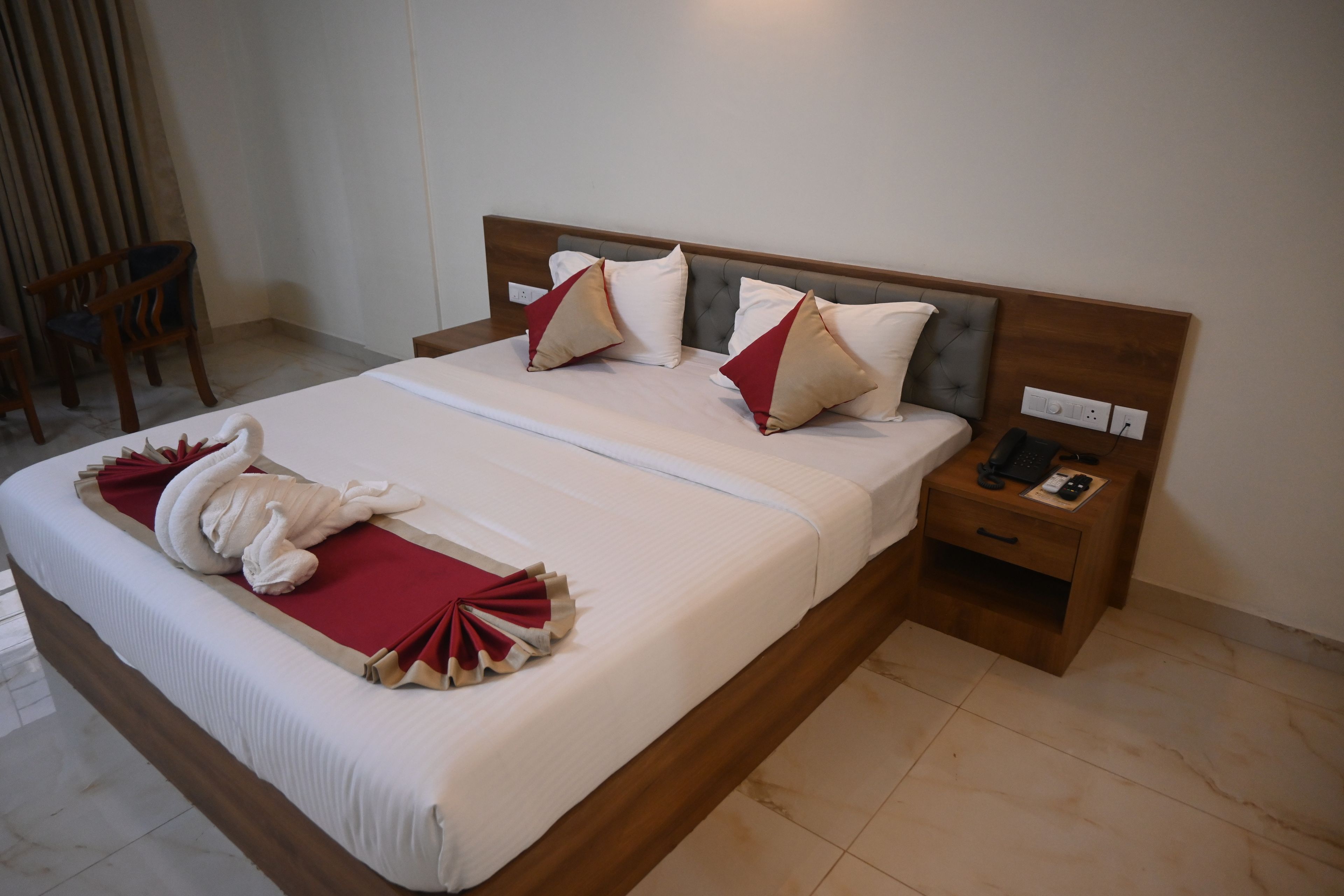A hotel room with a large bed, a wooden headboard, a bedside table with a phone, and a chair.