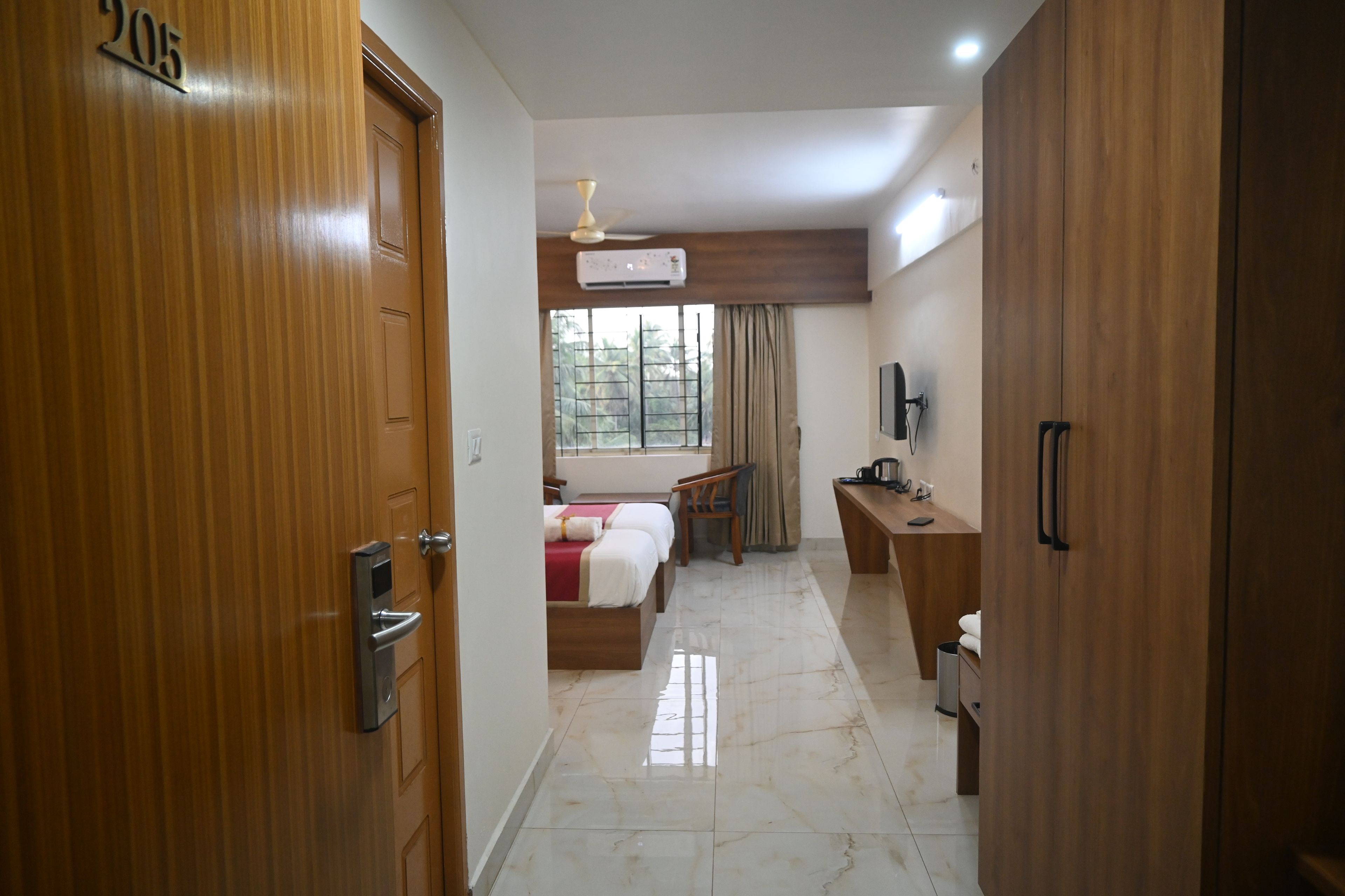 Habitación de hotel con puerta de madera, una cama, un escritorio, una silla, un televisor y una ventana con cortinas.