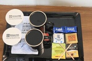 A tray with two black mugs, a black thermos, and various packaged food items including Amul dairy creamers, sugar packets, and tea.