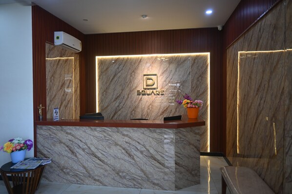 A reception desk with a marble wall, a logo, and a potted plant.