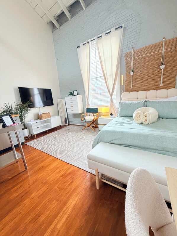 Un dormitorio moderno con cama, escritorio, televisor y ventana con cortinas.