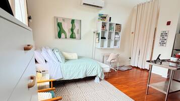 A bedroom with a bed, a desk, a chair, a wardrobe, a radiator, and a wall with a motivational quote.