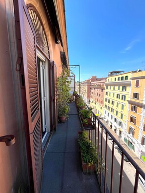 Ein Balkon mit Topfpflanzen, einem Metallgeländer und Blick auf angrenzende Gebäude.