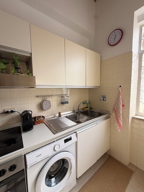 Eine kompakte Küche mit Waschmaschine, Spüle und einer Uhr an der Wand.