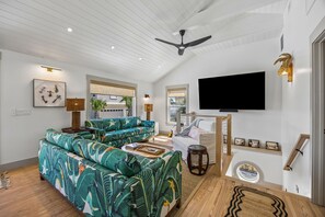 A modern living room with a large sofa, a flat-screen TV, and a ceiling fan. - Sunday Best - Steps from the beach (Fernandina Beach)