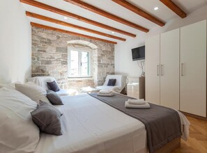 A bedroom with a stone wall, wooden beams, a bed, a chair, a TV, and a wardrobe. - Double bedroom with King sized bed and Old City View - A1 (Split)