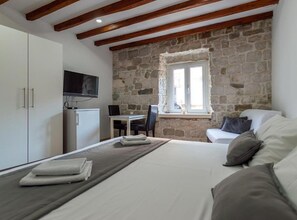 A bedroom with a bed, a TV, a stone wall, and a window. - Double bedroom with King sized bed and Old City View - A1 (Split)