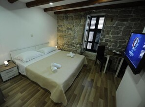 A bedroom with a bed, a nightstand, a desk, a television, and a stone wall. - Double Room with Separate beds and Old City View - A2 (Split)