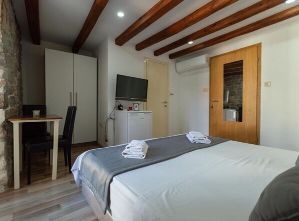 Una habitación de hotel con una cama, un escritorio con una silla, un televisor y un armario.