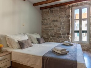A bedroom with a stone wall, a bed with white bedding, and a window with a view. - Double Room with Separate beds and Old City View - A2 (Split)