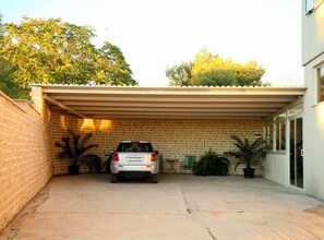 Een overdekte autocarport met een bakstenen muur, een geparkeerde auto en bloempotten.