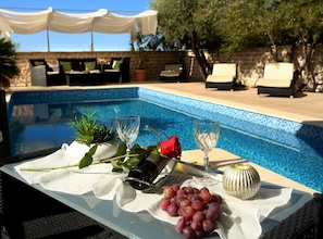 Un tavolo a bordo piscina con una bottiglia, bicchieri da vino, una rosa e grappoli d'uva.