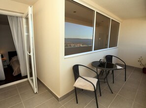 A balcony with a view of a body of water and distant land, a table with two chairs, and a potted plant. - Two Bedroom Apartment Sea View with Balcony (Okrug Gornji)