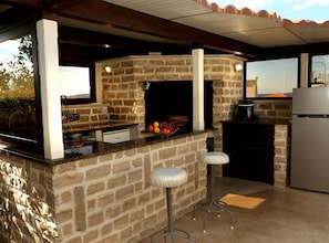 A stone-built outdoor kitchen with a grill, bar stools, and a refrigerator. - Two Bedroom Apartment Sea View with Balcony (Okrug Gornji)