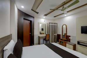A hotel room with a bed, a desk, a wardrobe, a mirror, and a ceiling fan. - Classic Anusuya Hotel (Bhubaneshwar)