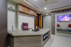 A reception desk with a laptop, a red chair, and a television displaying a list of songs. - Classic Anusuya Hotel (Bhubaneshwar)