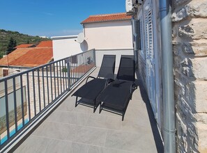 A balcony with two sun loungers and a table, overlooking a residential area with red-tiled roofs. - Two Bedroom Holiday Home with Outdoor Swimming Pool (Murter)
