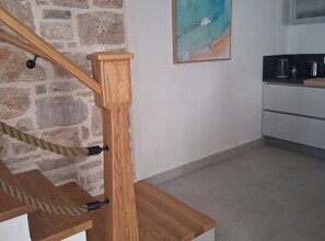 Eine Holztreppe mit Seilgeländer, eine Steinmauer und ein Küchenbereich mit Schränken und Geräten.