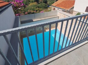 A residential balcony with a swimming pool, stone walls, and a view of a garden with pink flowers. - Two Bedroom Holiday Home with Outdoor Swimming Pool (Murter)