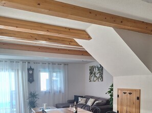 A room with a sloped ceiling, wooden beams, a dining table with chairs, a sofa, a clock, and a door. - Two Bedroom Holiday Home with Outdoor Swimming Pool (Murter)