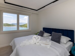 A hotel room with a large bed, a view of a lake, and a blue headboard. - Six Bedroom Sea View Villa with Two Swimming Pools (Blace)