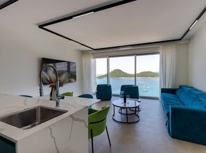 A modern living room with a sofa, chairs, a dining table, and a kitchen area with a sink and a vase of flowers. - Six Bedroom Sea View Villa with Two Swimming Pools (Blace)