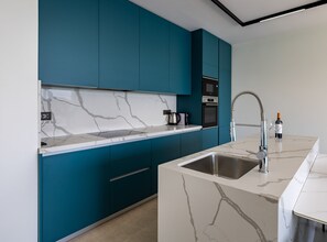A modern kitchen with teal cabinetry, a marble countertop, and stainless steel appliances. - Six Bedroom Sea View Villa with Two Swimming Pools (Blace)