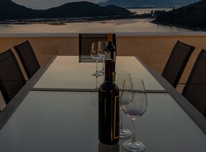 A table set for dining with a bottle and glasses, overlooking a scenic view of a river and mountains. - Six Bedroom Sea View Villa with Two Swimming Pools (Blace)