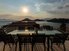 A glass-top table with chairs on a deck overlooking a body of water with mountains in the distance. - Six Bedroom Sea View Villa with Two Swimming Pools (Blace)