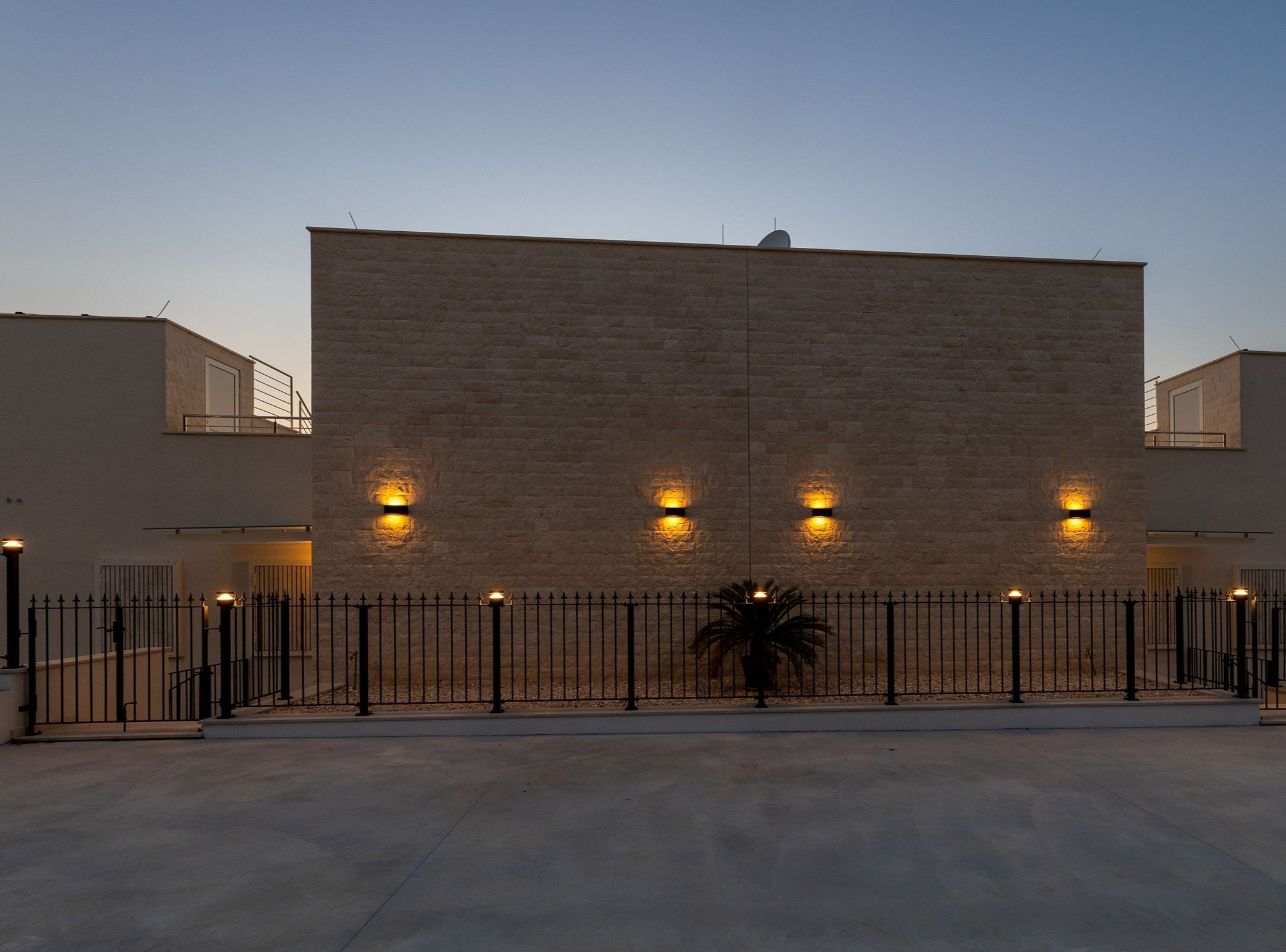 En moderne bygning med flad facade, jævnt fordelte lys og et metalhegn foran.