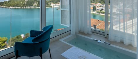 A balcony with a view of a lake and mountains, a blue chair, and a small pool.