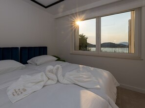 A bedroom with a large bed, a headboard, and a window with a view of a body of water and hills. - Six Bedroom Villa with Sea View & Two Pools (Blace)