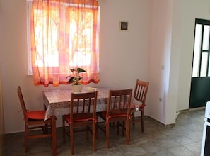A dining area with a table and four chairs, a window with sheer curtains, and a potted plant on the table. - Two-Bedroom Apartment in Ground Floor with Terrace (Orebic)