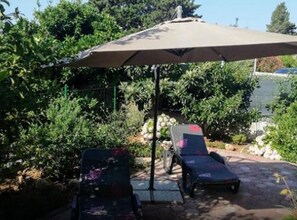 A patio with two lounge chairs and a large umbrella, surrounded by lush greenery and a body of water. - Two-Bedroom Apartment with Garden View (Orebic)