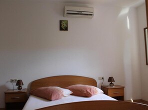 A bedroom with a bed, two bedside tables with lamps, an air conditioner, and a small painting on the wall. - Two-Bedroom Apartment with Garden View (Orebic)