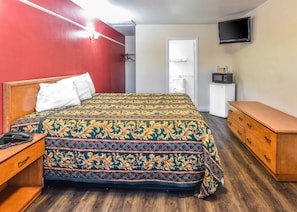 A hotel room with a bed, a wooden dresser, a television, and a small refrigerator. - Sunset Motel (Pomona)