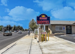 Letrero de motel con un sol, cielo despejado y una calle con coches.