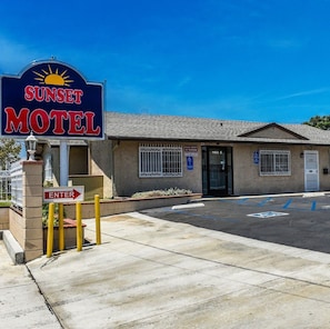 Un motel con un letrero que dice 'Sunset Motel', un estacionamiento con espacios para discapacitados y una entrada con portón.
