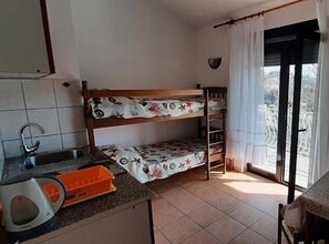 A compact kitchen with a sink, a toaster, and a small orange container. There is a bunk bed with a patterned bedspread. - Two Bedroom with Balcony (A3) (Marina)