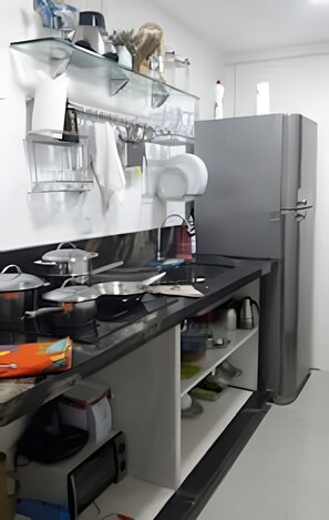 A modern kitchen with a stainless steel countertop, a refrigerator, and various kitchen appliances. - Casa Praia das Dunas (Cabo Frio)