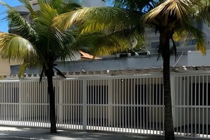 A fenced area with palm trees, a building with a flat roof, and a white railing. - Casa Praia das Dunas (Cabo Frio)