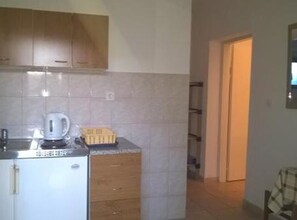 A compact kitchen with a refrigerator, a coffee maker, and a toaster. There is a wooden cabinet above the counter and a tiled backsplash. - Three Bedroom Apartment with Terrace (A2) (Marina)